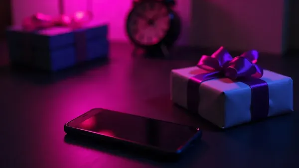 Smartphone vedle malého dárku s fialovou mašlí, na tmavém stole (ilustrace k článku)